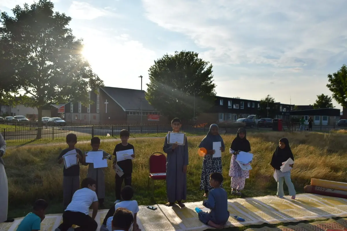 Children holding their certificates on the grass in the late afternoon sun